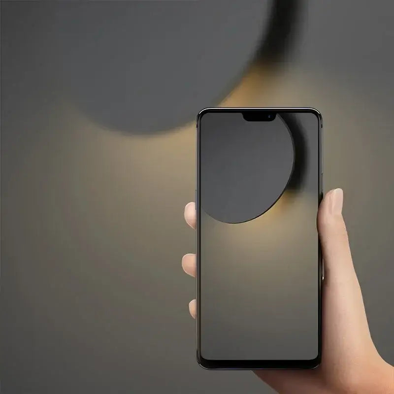 Black smartphone with sleek minimalist design and circular cutout paired with modern white curved led wall lamp for bedroom