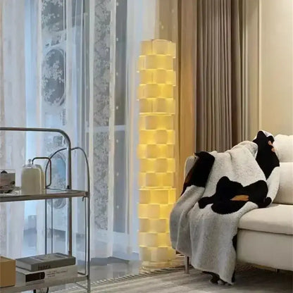 Modern white cylindrical vertical floor lamp with stacked cube design emitting warm yellow light for living room use