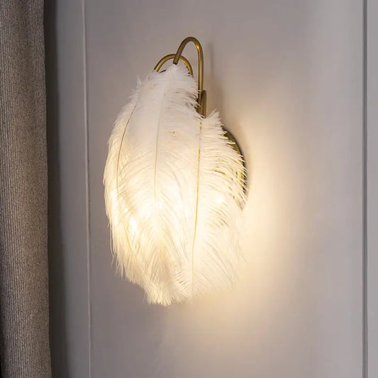 Modern white feather metal wall sconce with a luminous white feather and gold-toned metal frame for bedroom lighting