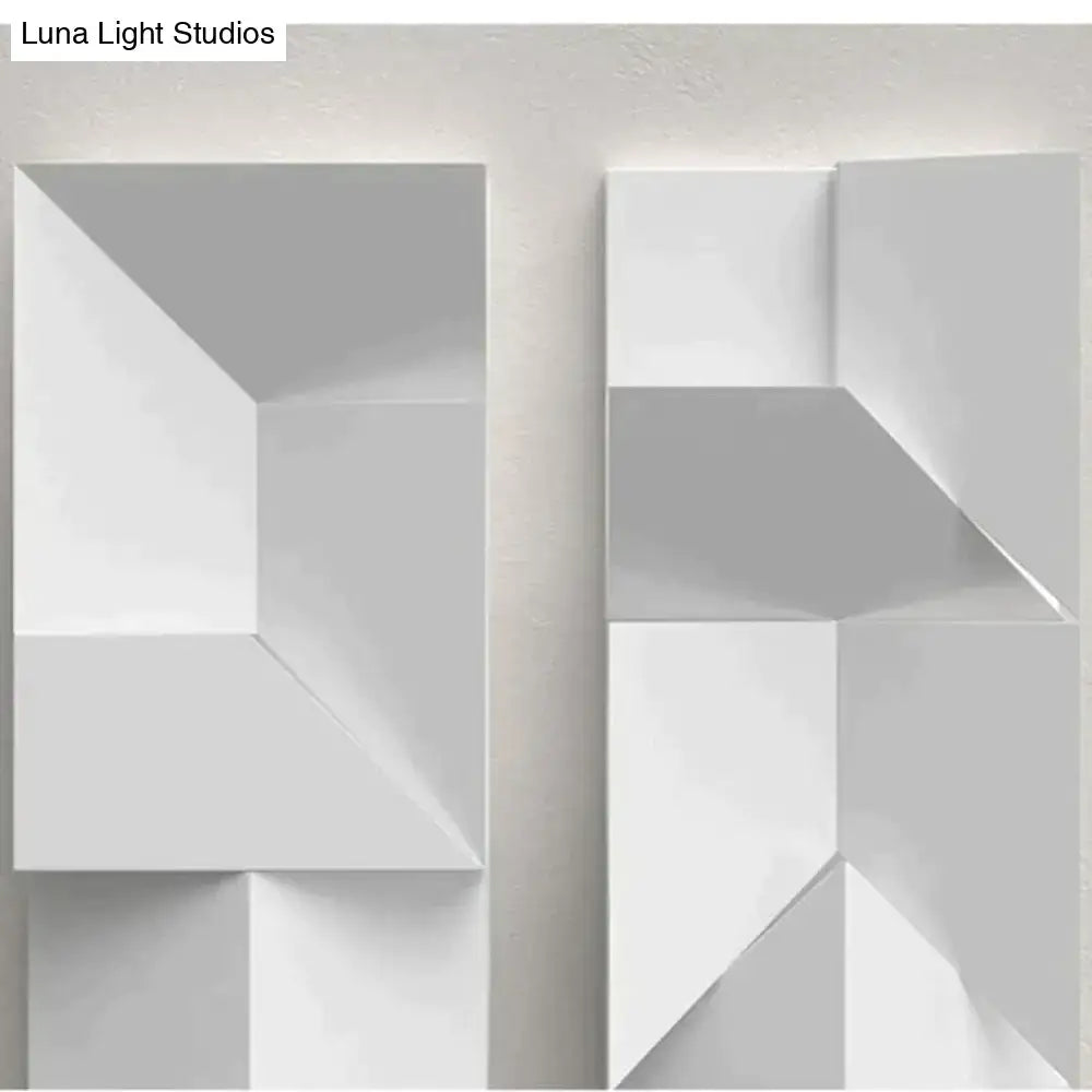 Modern white geometric wall lamp with angular three-dimensional panels illuminated in a living room setting