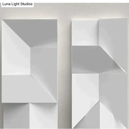 Modern white geometric wall lamp with angular three-dimensional panels illuminated in a living room setting