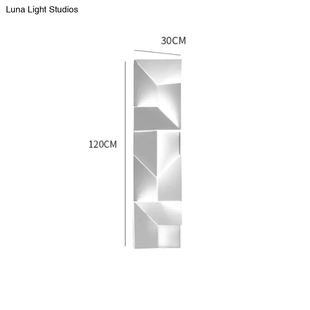 Modern white geometric wall lamp in polished metal illuminated in a living room setting with angular design