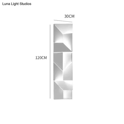 Modern white geometric wall lamp in polished metal illuminated in a living room setting with angular design