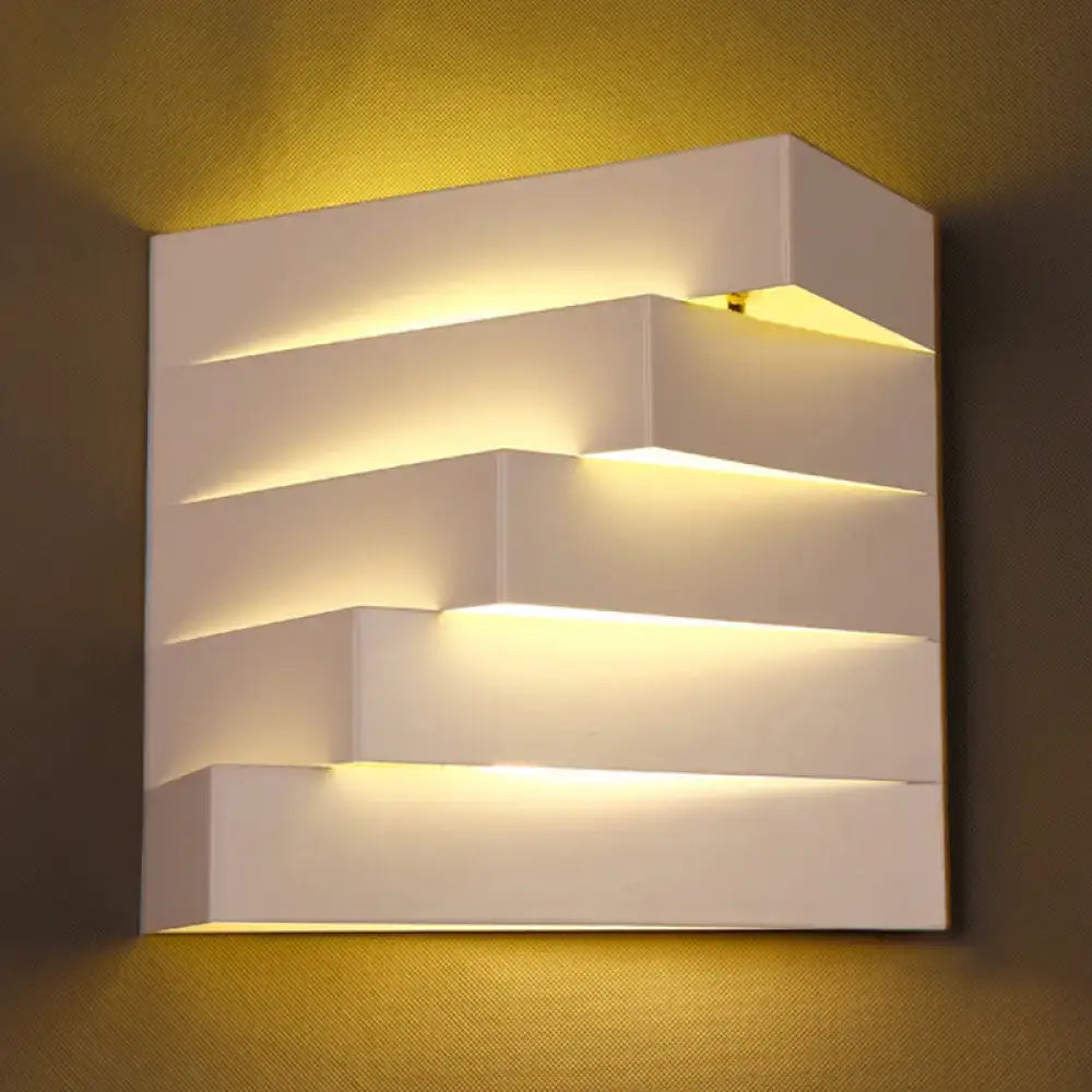 Modern white geometric wall mounted lighting sconce with layered stepped design emitting warm ambient light