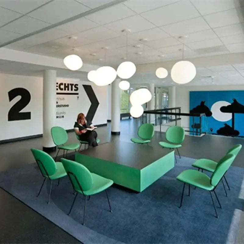 Modern white glass ball led pendant light hanging above mint-green upholstered chairs with black metal frames in office space decorbites glass ball