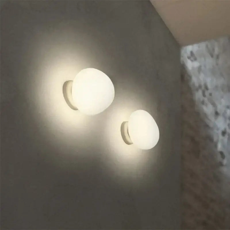 Two minimalist white glass egg wall sconces with frosted globe design and sleek metallic bases for bedroom wall lamp