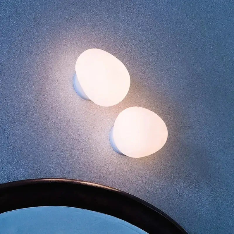 Two modern white glass egg wall sconces emit a warm glow as a bedroom wall lamp on a textured blue wall