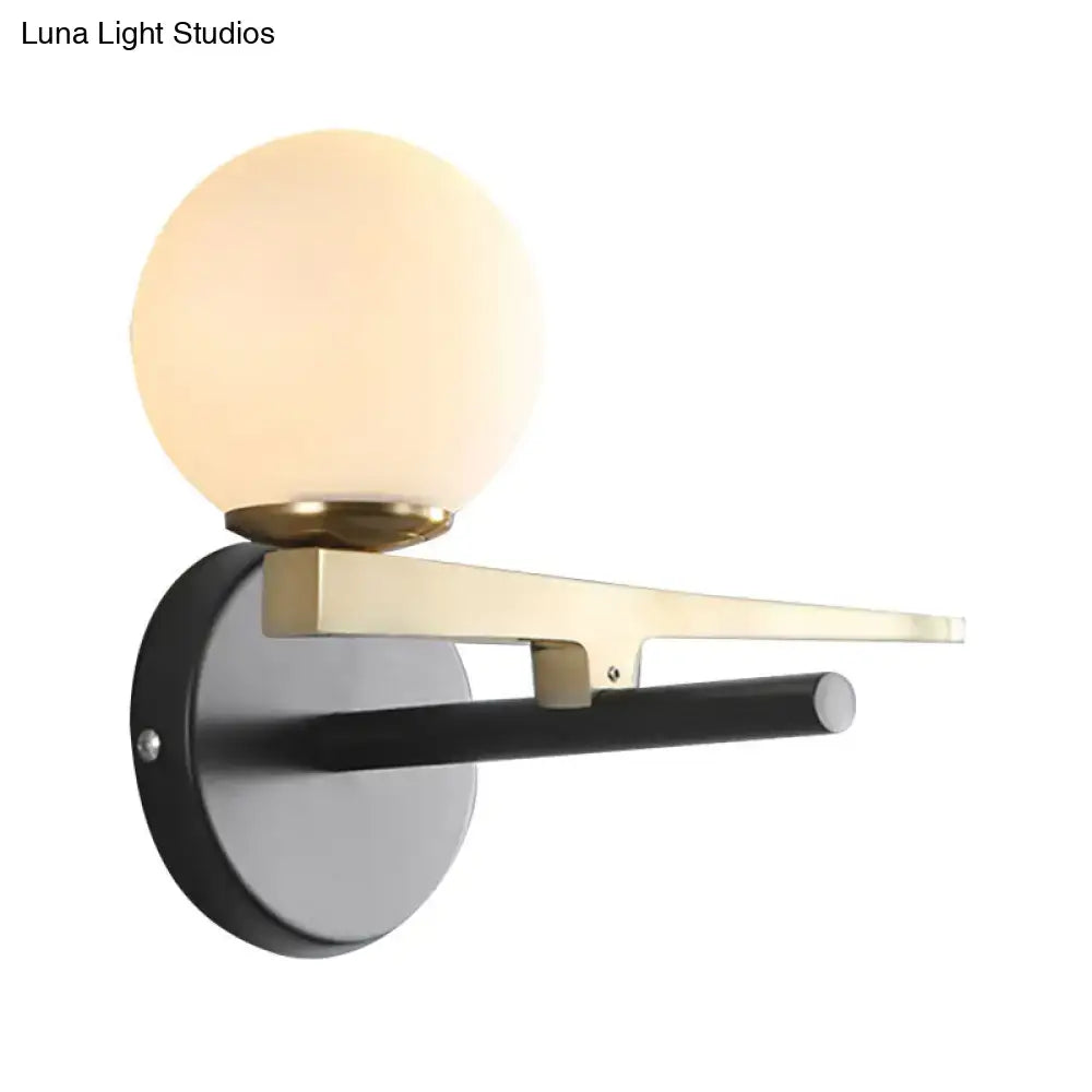 Modern wall light featuring a single light with white frosted glass globe, brass accents, and black metal mounting plate