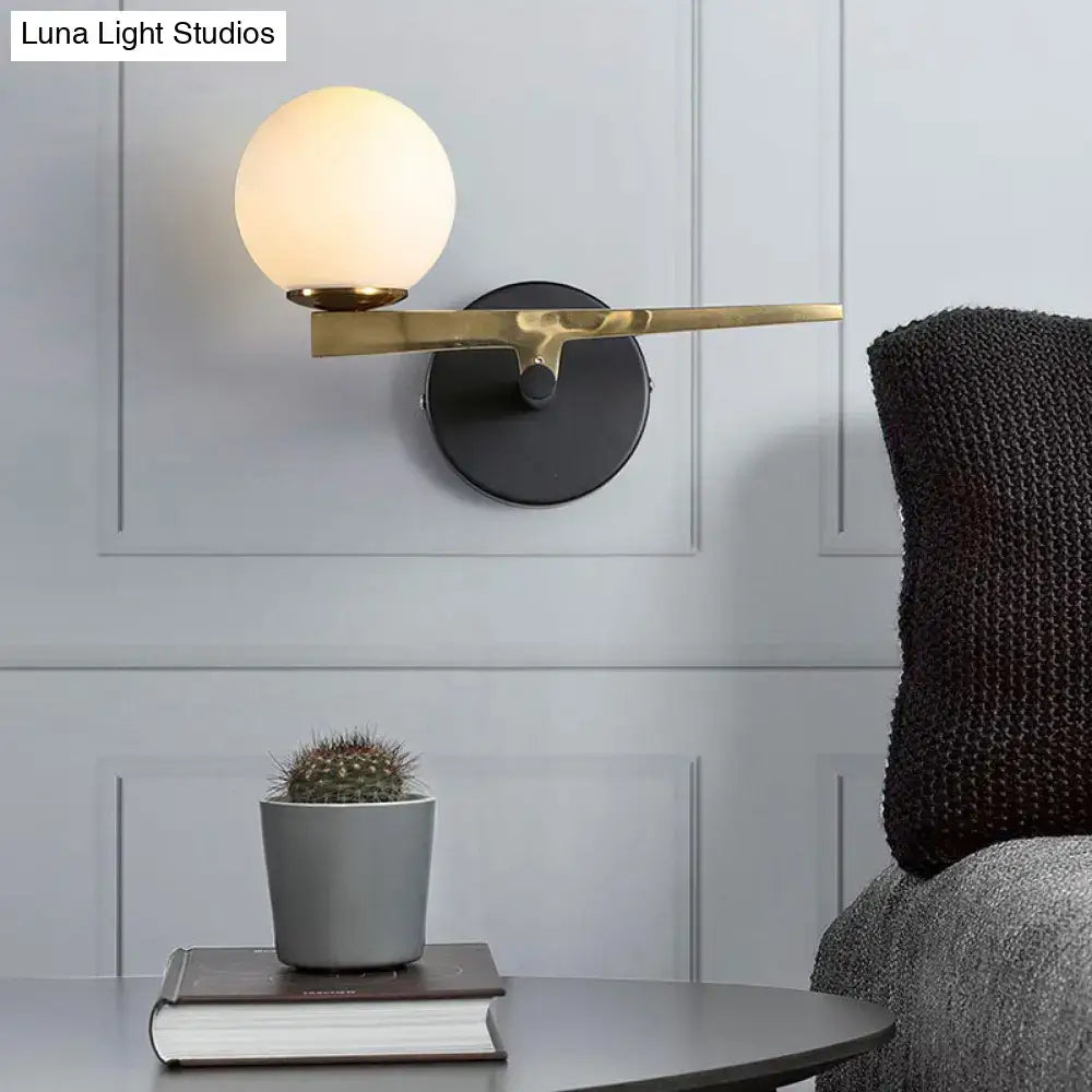 Modern brass wall light with frosted white glass globe shade featuring gold and black single light design for bedroom