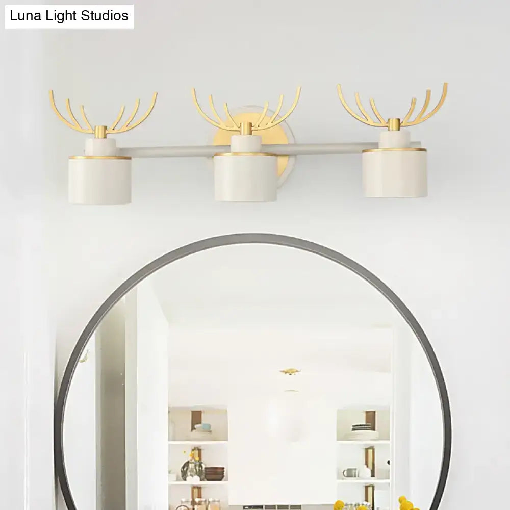 Set of three modern white and gold antler wall light fixtures with cylindrical shades on a sleek silver bar for bathroom vanity