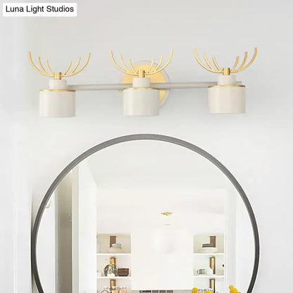 Set of three modern white and gold antler wall light fixtures with cylindrical shades on a sleek silver bar for bathroom vanity