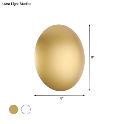 Gold-colored oval wall light with smooth metallic finish in white gold providing warm white illumination for bedrooms