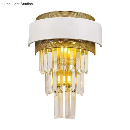 Modern wall sconce with white and gold metallic frame and cascading clear crystal prisms emitting warm light