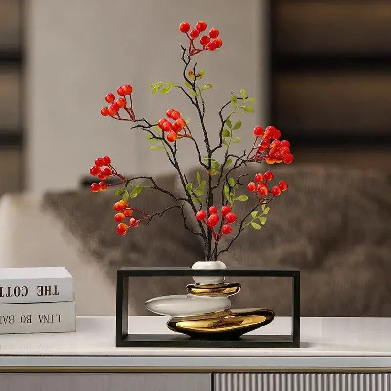Modern white and gold ceramic vase with sleek layered design holding artificial red berries in geometric golden rockery decorbites