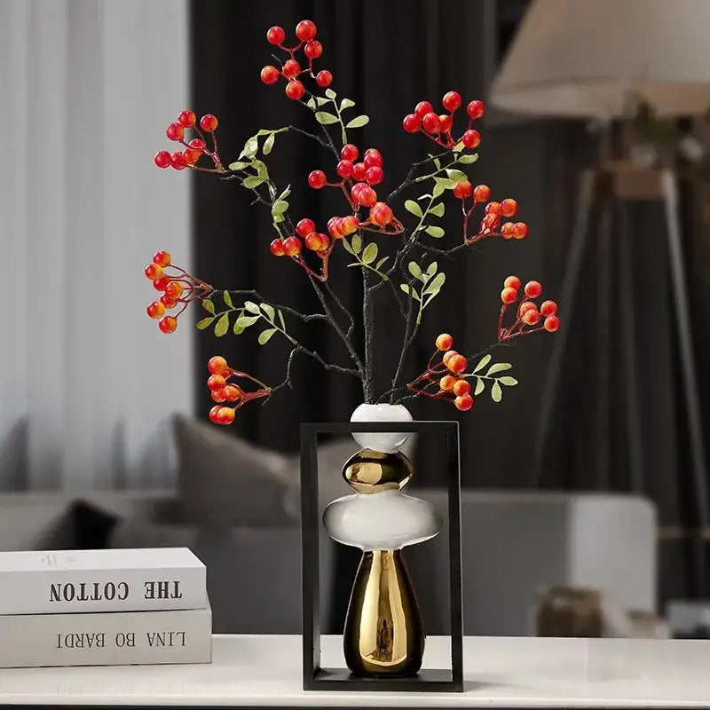 A modern white and gold ceramic vase with a tiered geometric golden rockery design holding red berry branches