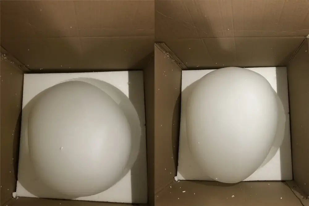A smooth matte white gregg glass suspension pendant light resting on foam inside a cardboard box for villa staircase