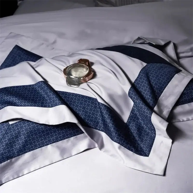 A rose gold-tone watch on a luxury white and navy egyptian cotton bedding set with geometric patterns