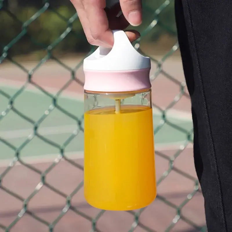 A clear glass electric protein shaker bottle with a white and pink silicone lid filled with orange juice
