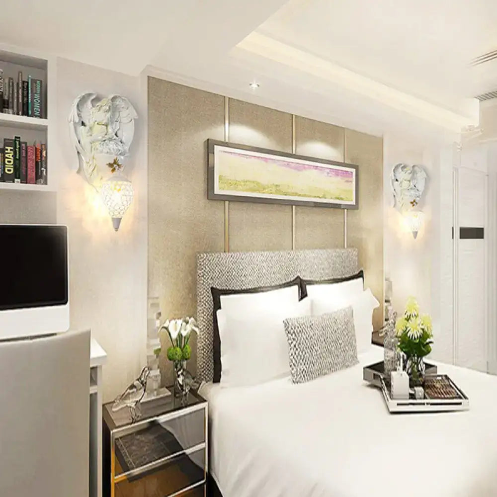 Modern white resin angel wall light with crystal shade mounted on a silver textured headboard with black trim in bedroom
