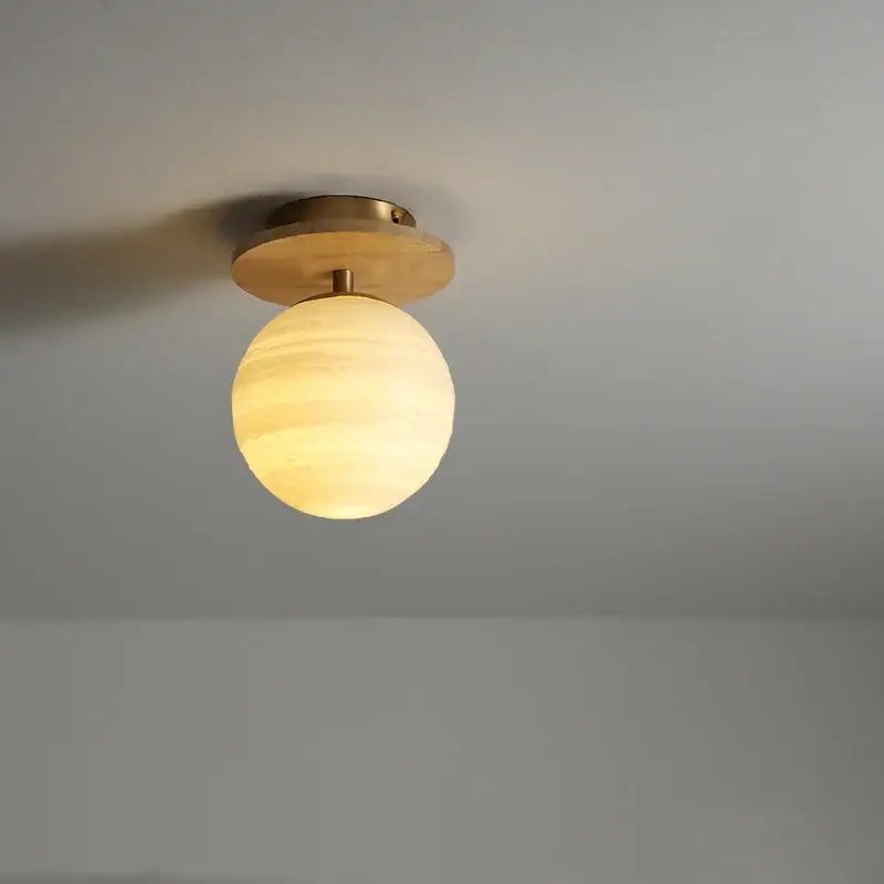 A warm spherical glass globe ceiling light with brass finish mounted on modern white decorbites ceramic wood led fixture