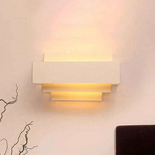 Modern white tiered rectangle wall lamp with layered stepped design emitting warm light for bedroom wall sconce use