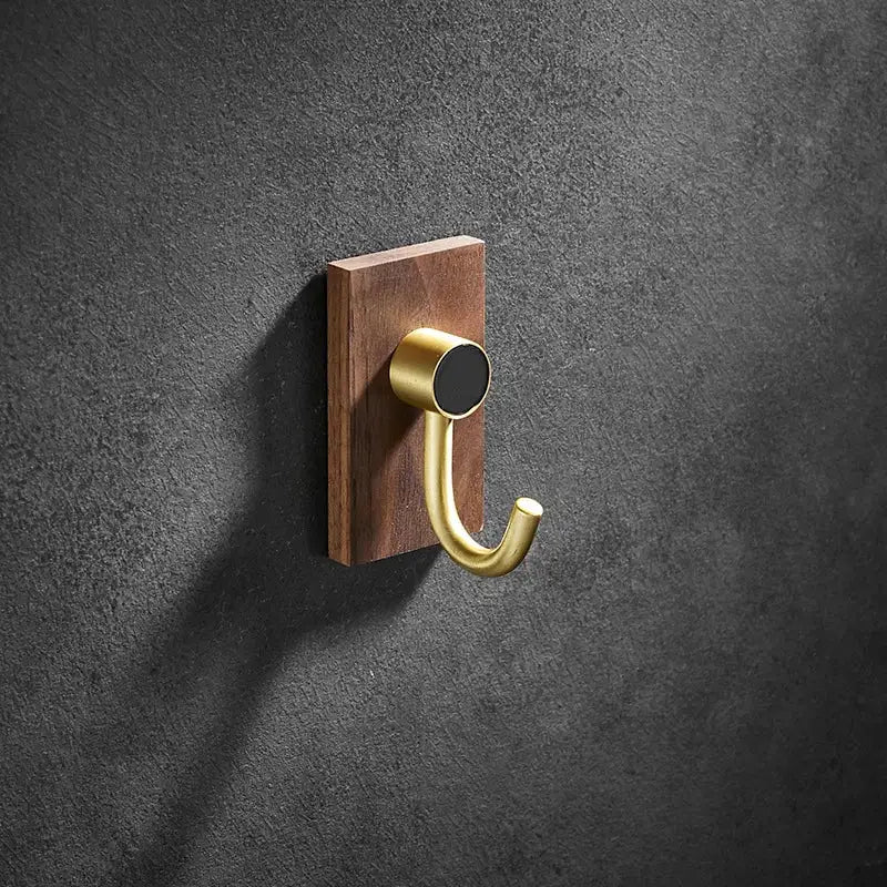 A sleek brushed gold wall hook with a rectangular walnut base mounted on a dark textured wall decorbites brass brushed