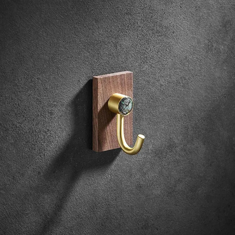 A modern wood and brushed gold wall hook with polished brass, walnut plate, and greenish black abalone shell accent