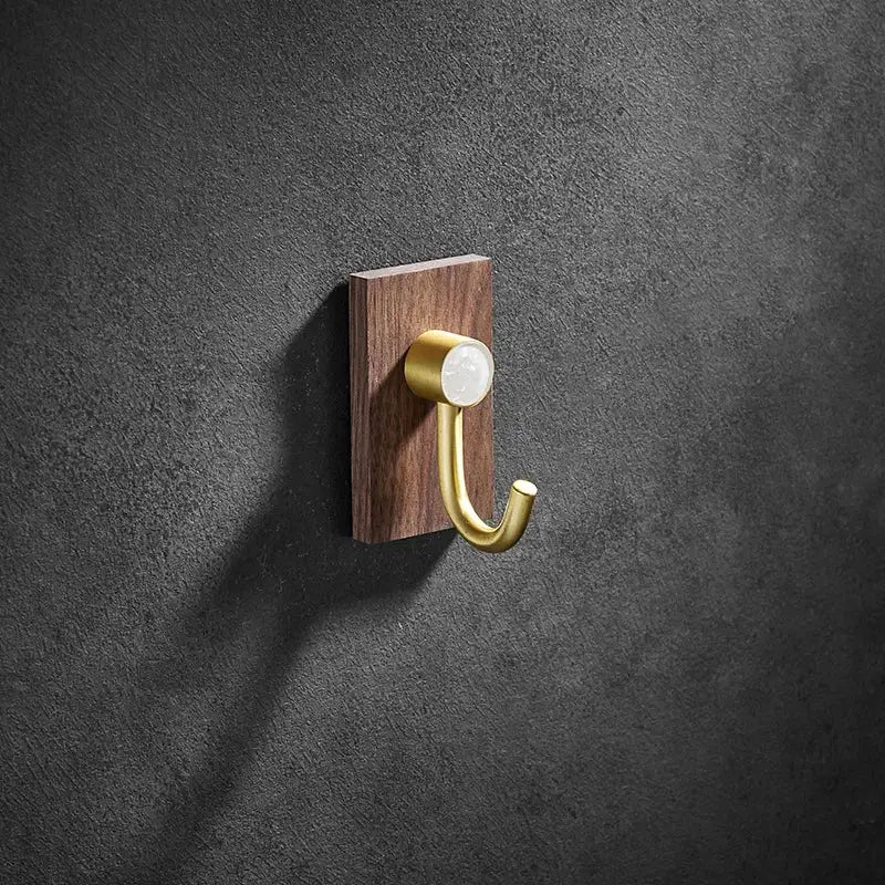 A modern wood and brushed gold wall hook with a sleek brass brushed finish mounted on a dark wood plaque for kitchen decorbites