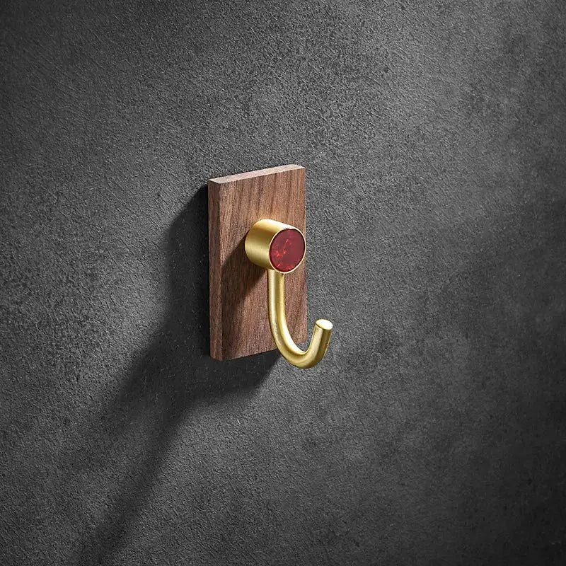 A sleek modern wood and brushed gold wall hook with a red accent mounted on dark wood plaque by decorbites brass brushed