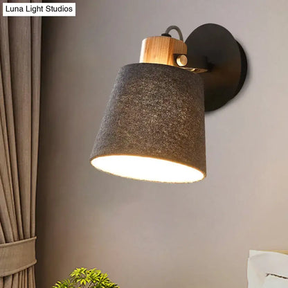 Modern wood and gray fabric shade wall lamp with a warm-toned light, natural wood accent, and matte black metal base