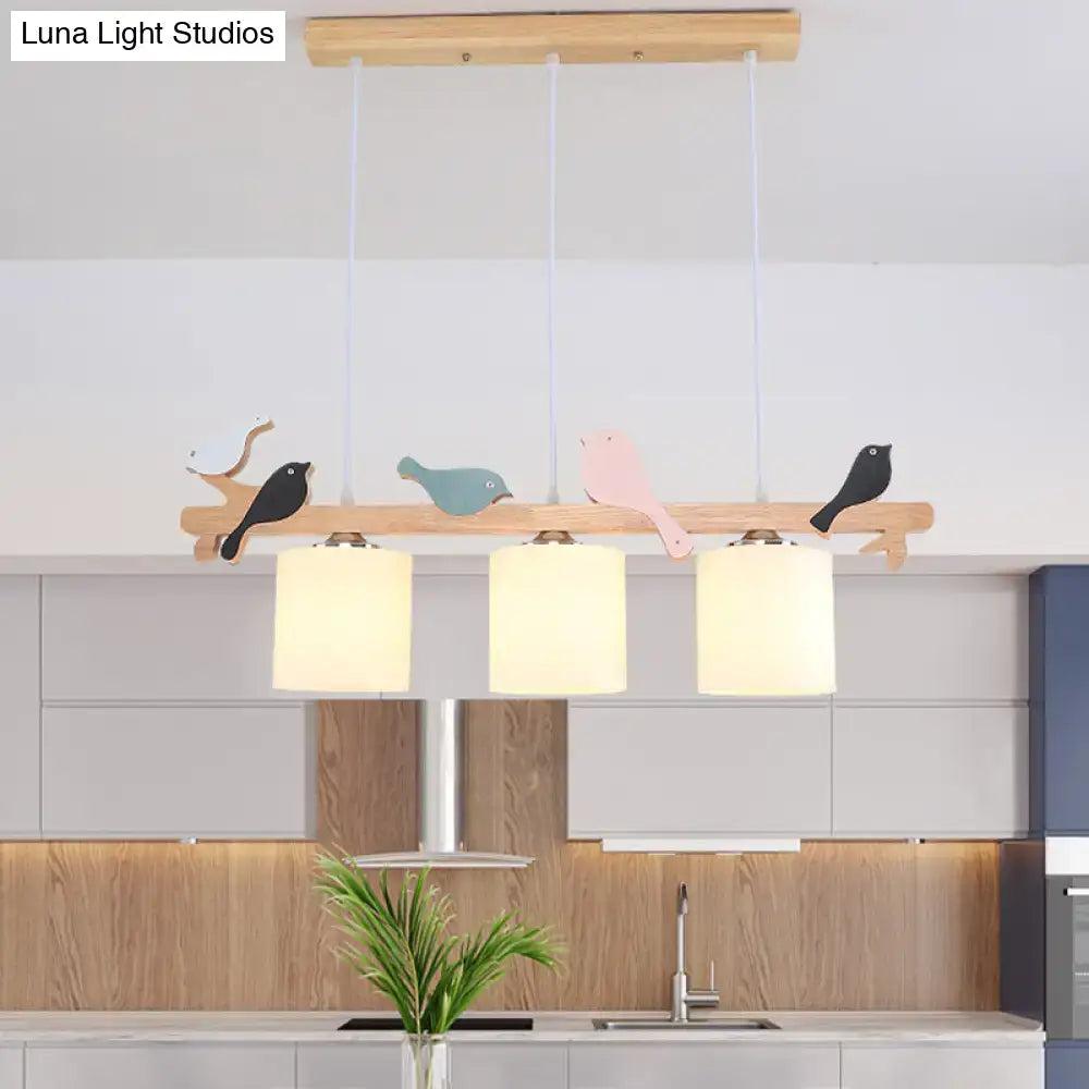 Wooden pendant light with three frosted glass shades and colorful bird cutouts on a natural wood barrel island beam
