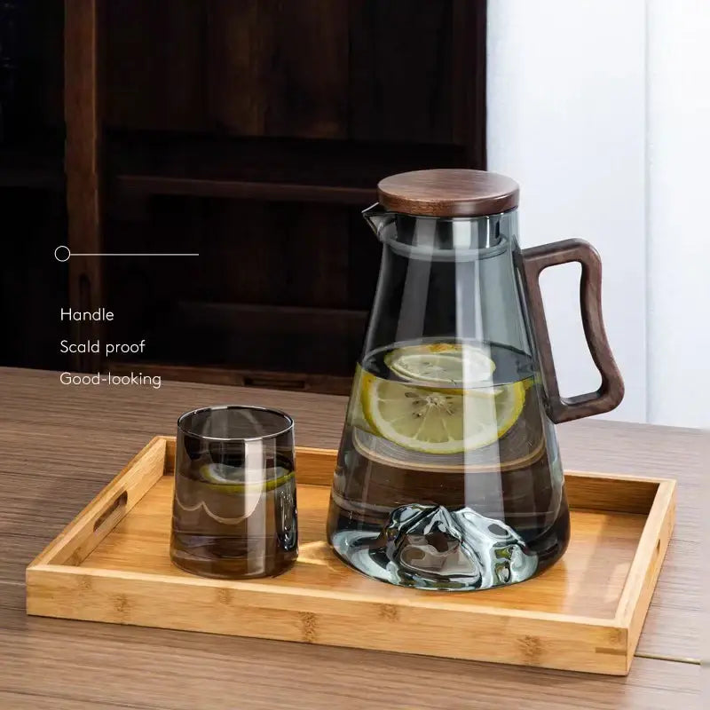 Modern wood handle glass cold water jug with clear glass and dark wood lid filled with water and lemon slices