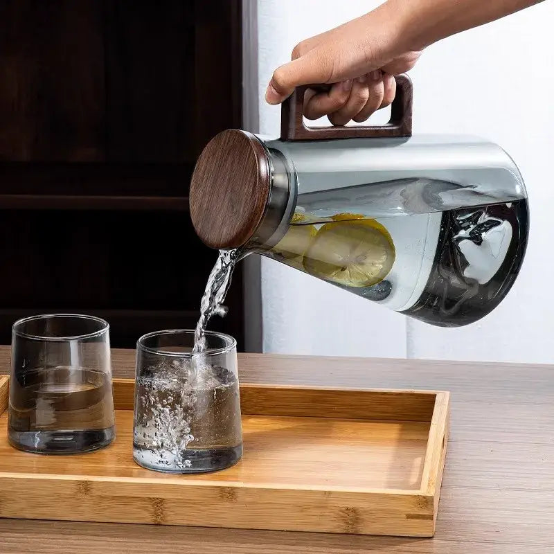 Modern glass cold water jug with clear glass body and dark wood handle filled with lemon-infused water