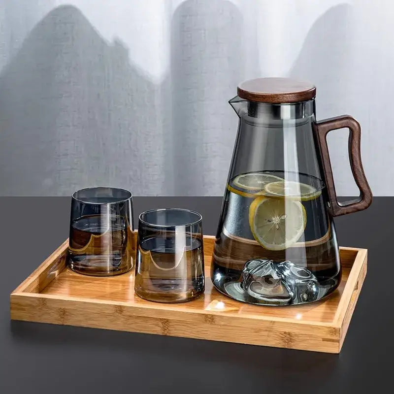 Clear glass cold water jug with wooden lid and handle filled with lemon-infused water and ice cubes