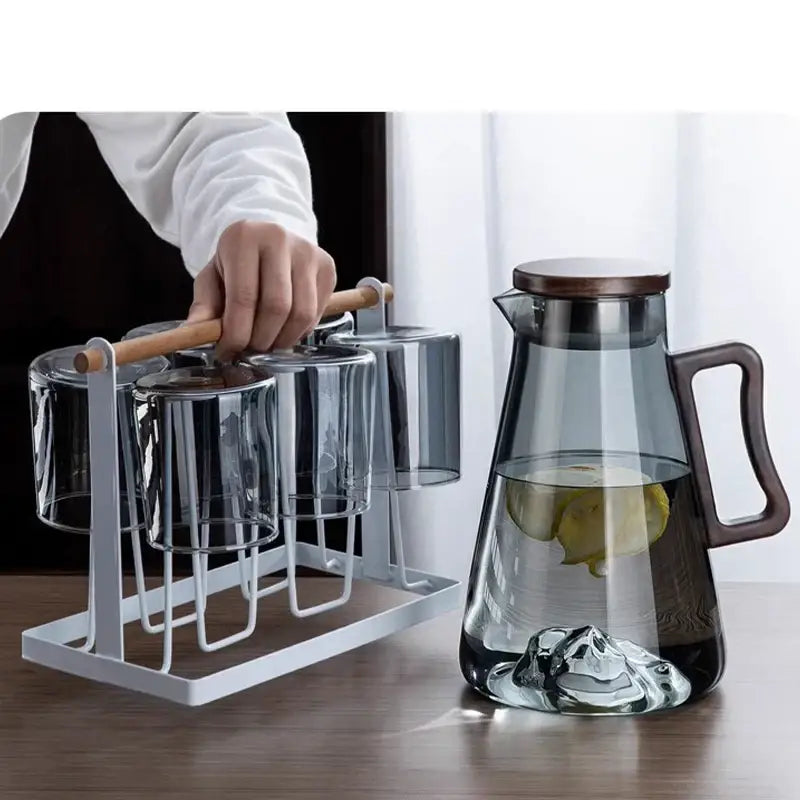 Transparent glass cold water jug with dark wooden lid and handle filled with water and lemon slices for kitchen use