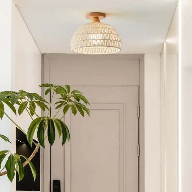 A modern woven beige decorbites led wicker wood ceiling light with wooden base hangs above a gray door