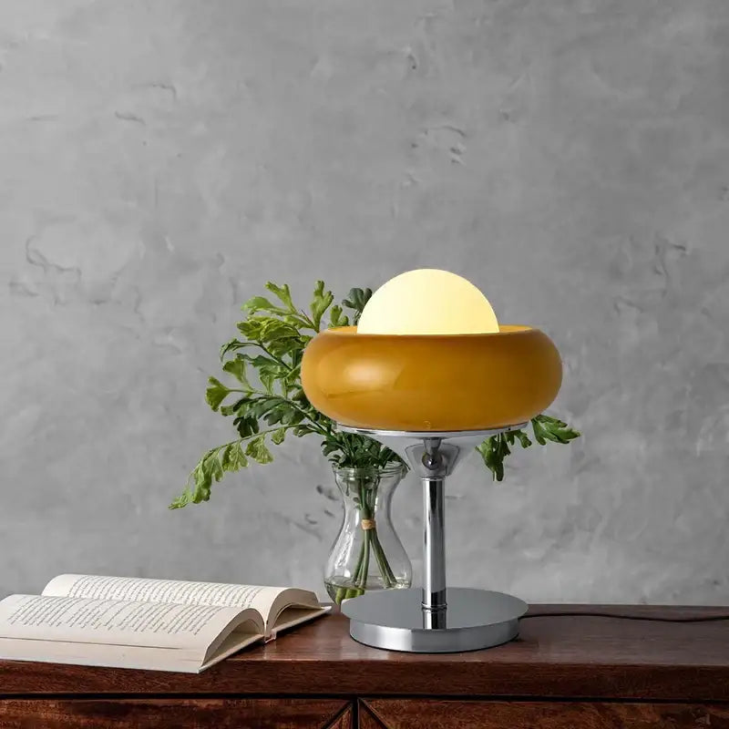 A sleek mustard-yellow glass egg tart desk lamp with chrome base and soft glowing bulb for modern bedroom use