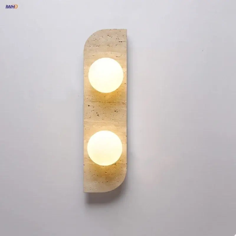 Modern yellow travertine led wall lamp with two warm circular bulbs set into a textured beige stone panel for bedroom