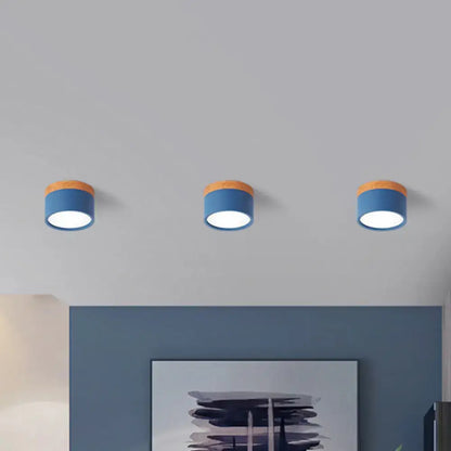 Three decorbites flush mount ceiling lights with blue metal shades and wooden tops emitting soft white glow for kitchen bar