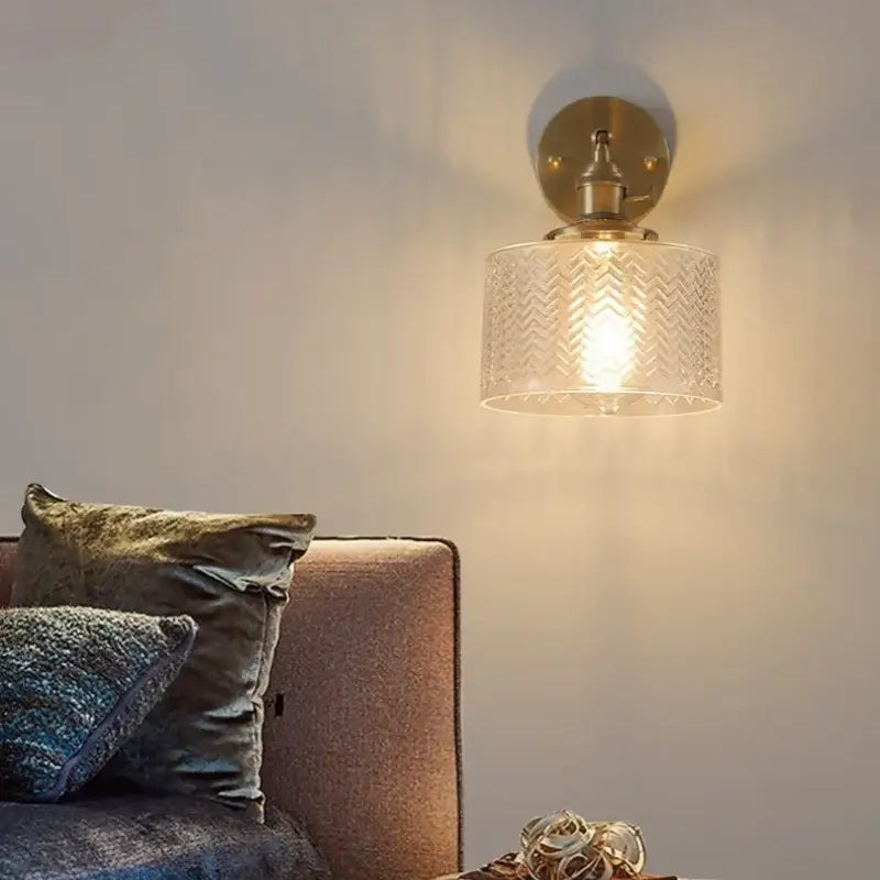 A brass wall lamp with a green glass led clear shade featuring an etched chevron pattern for bedroom use