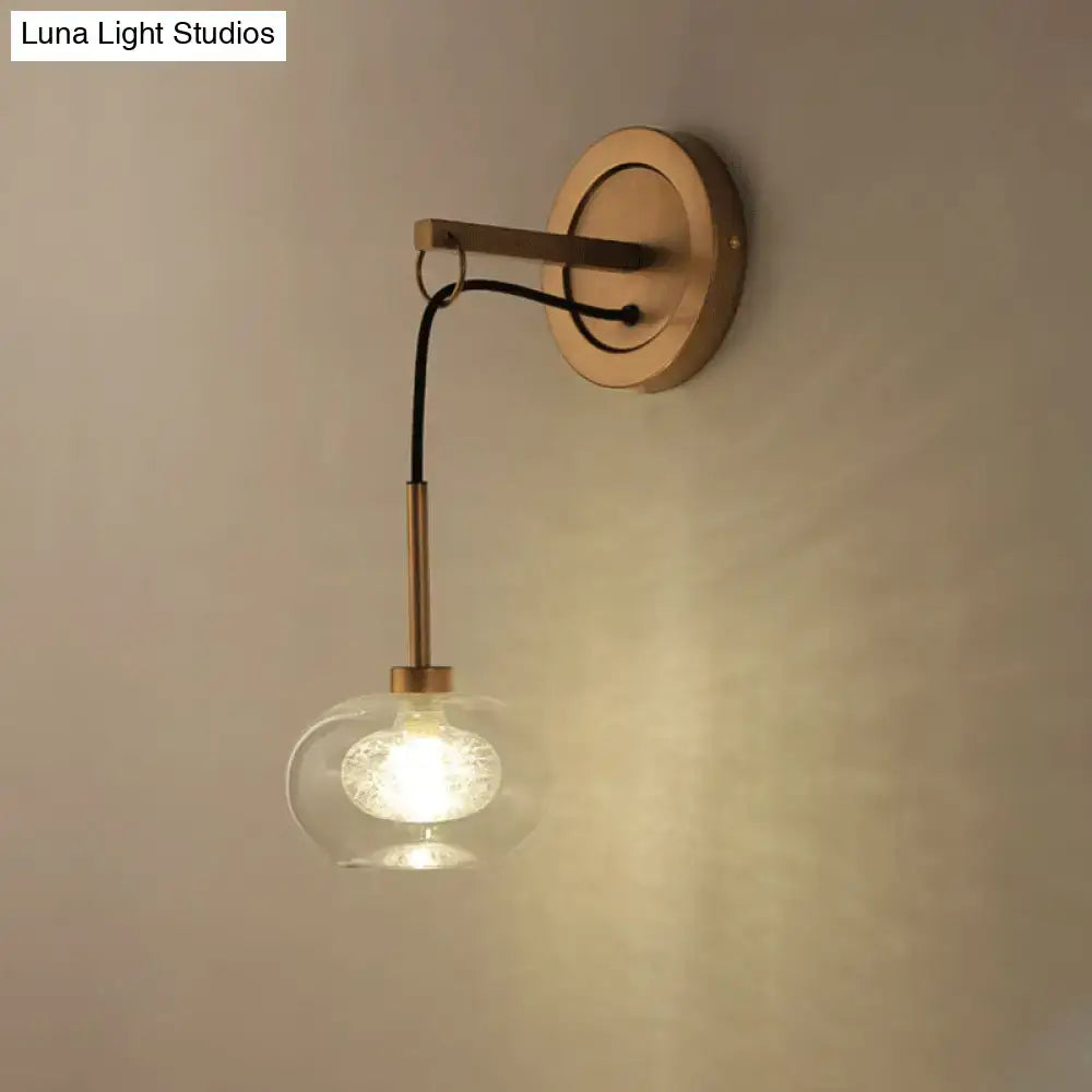Brass-finished modernist wall sconce with clear amber white glass globe housing an illuminated bulb for bedroom use