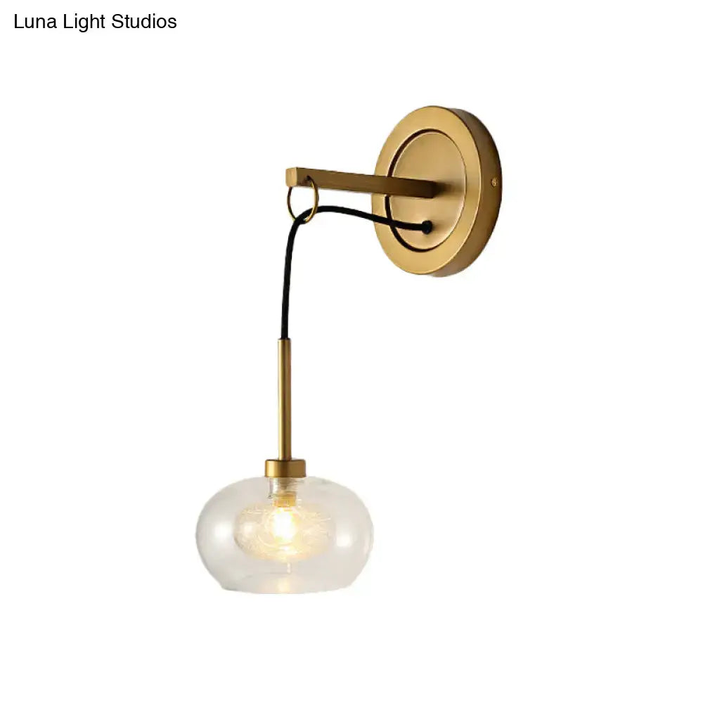 Gold-toned modernist wall sconce with amber white glass globe shade and black cord for bedroom lighting