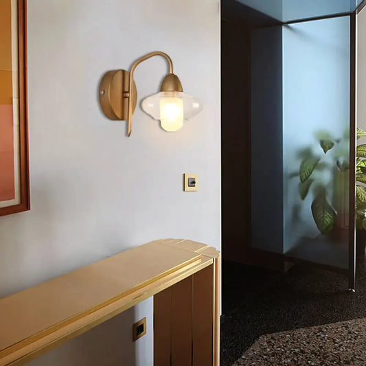 Modernist brass wall lamp with frosted clear glass shade and visible bulb base for bedroom sconce lighting