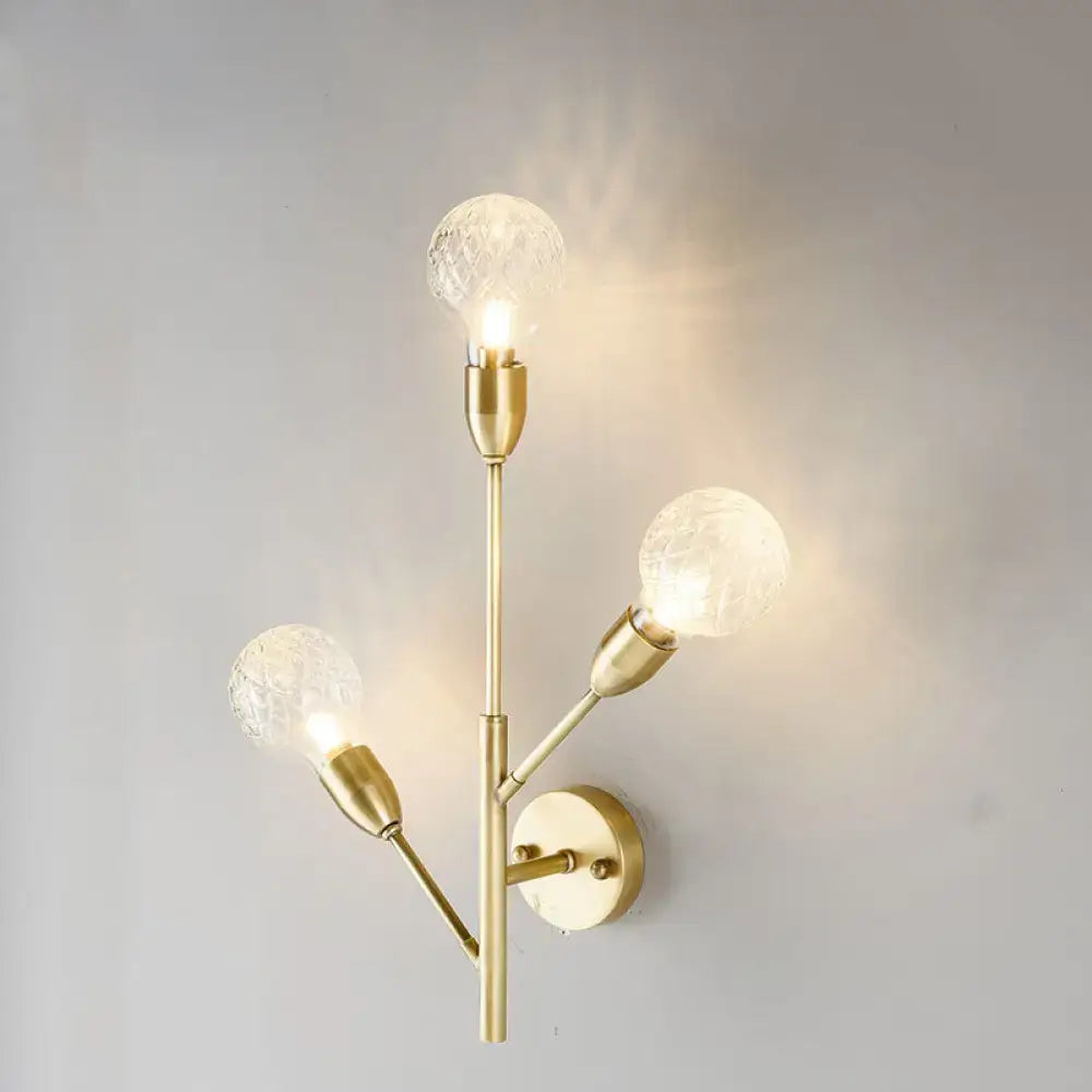 Modernist brass wall mount light fixture with three textured prismatic glass globe bulbs for bedroom use