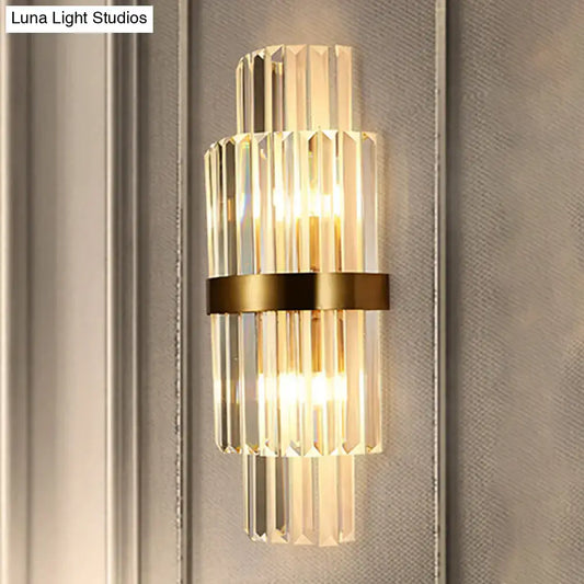A modernist gold and clear crystal cylinder wall lighting fixture with vertical rods and a sleek brass band for living room