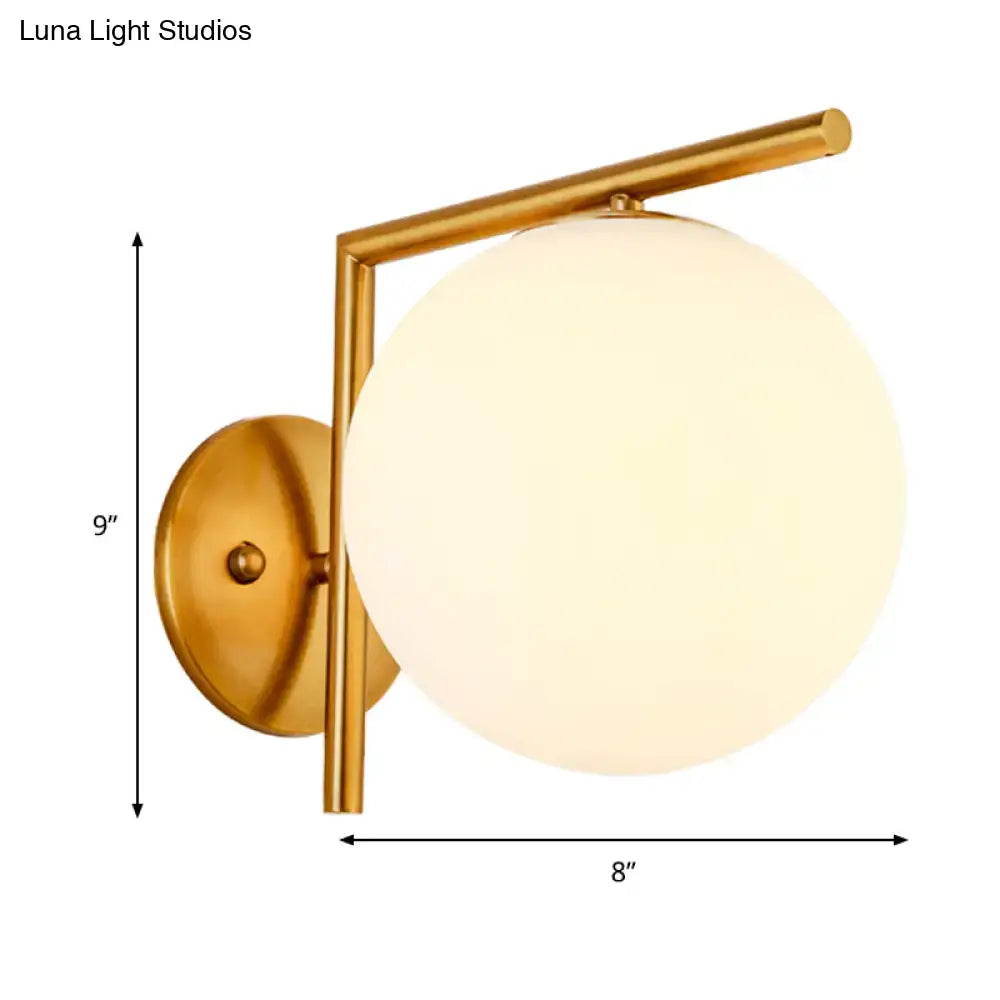 Modernist gold and white globe sconce light with frosted glass globe and minimalist geometric frame for bedroom wall lamp