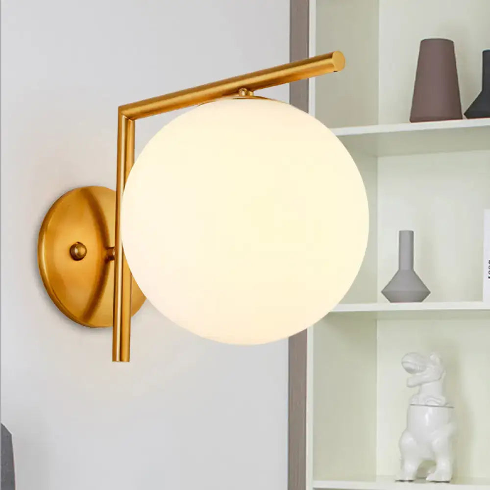 Modernist gold-toned globe sconce light with a frosted white glass globe for bedroom wall lighting