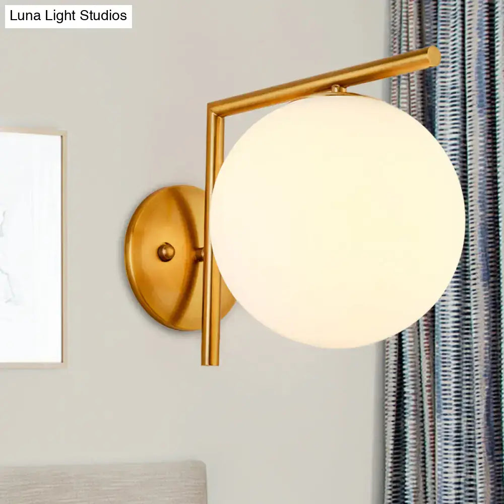 Modernist gold and white globe sconce light with a gold-toned metal frame and frosted glass globe for bedroom walls