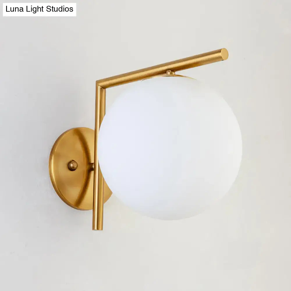 Modernist gold and white globe sconce light with frosted glass shade and geometric metal frame for bedroom wall use