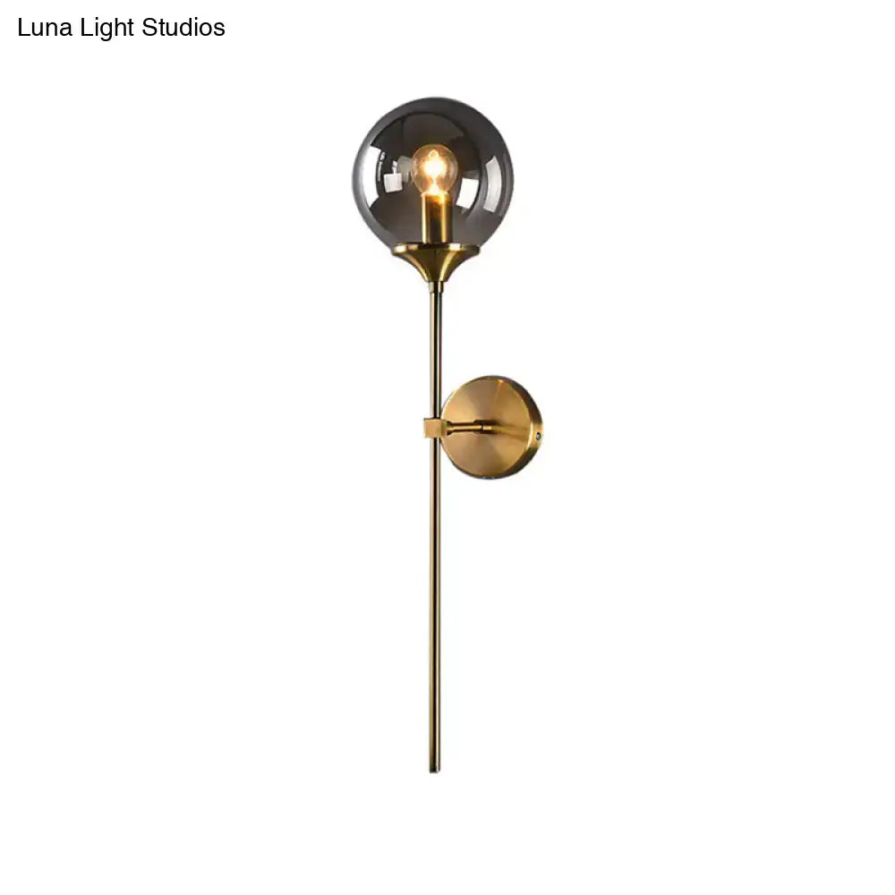 A sleek modernist brass-finished glass round sconce lamp with a smoked globe and exposed filament bulb for living room